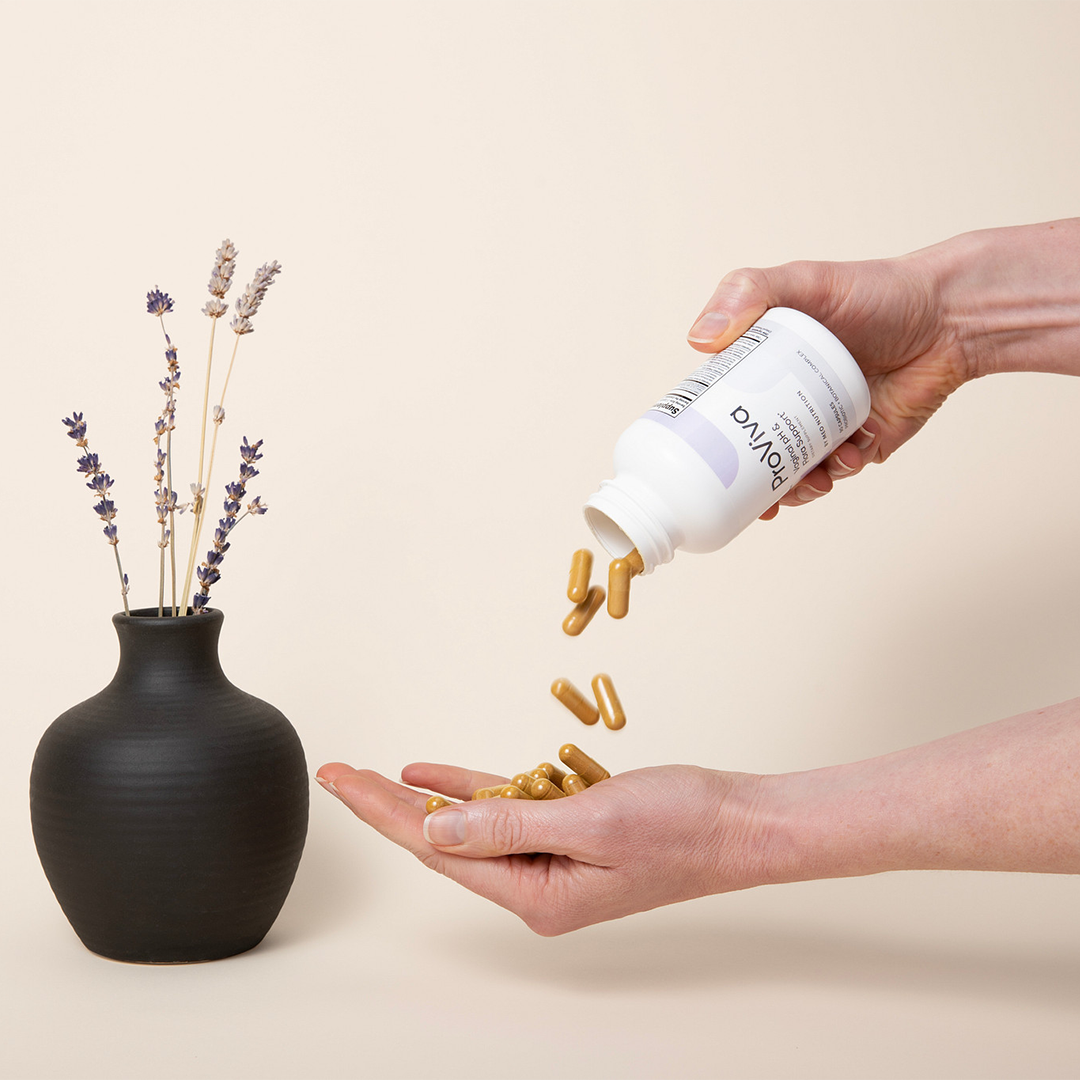 Person pouring supplements from a bottle into their hand next to a black vase with lavender.